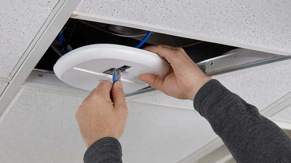 Illustrative technician connecting a terminated Cat6 cable to a ceiling Wi-Fi access point